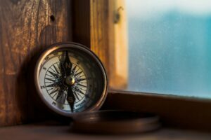 A close-up of a vintage compass resting on a wooden window sill. The compass is a symbol of direction and guidance, and it can serve as a metaphor for defining purpose in strategy. Photo by Jordan Madrid on Unsplash {{brizy_dc_image_alt entityId=