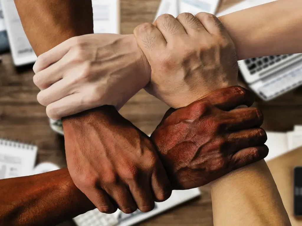 Team-2 Team alignment concept with four diverse hands interlocked in unity, symbolising collaboration, trust, and cohesion in a professional workspace.