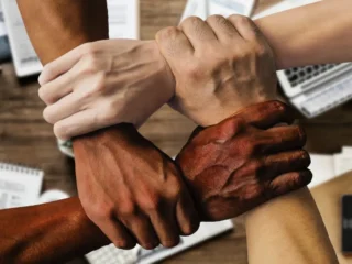 Team alignment concept with four diverse hands interlocked in unity, symbolising collaboration, trust, and cohesion in a professional workspace.