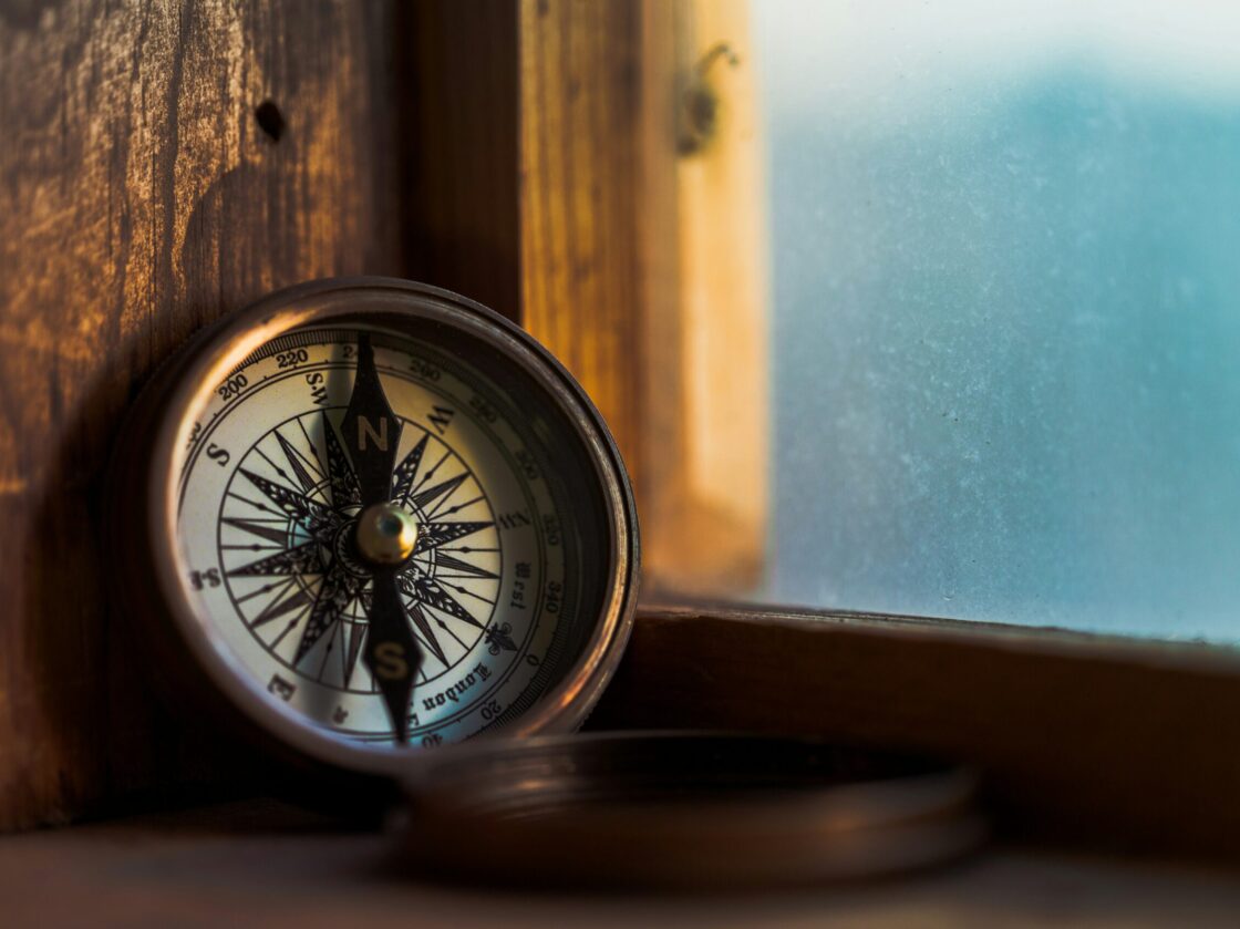 jordan-madrid-iDzKdNI7Qgc-unsplash How to define your company purpose — A close-up of a vintage compass resting on a wooden window sill. The compass is a symbol of direction and guidance, and it can serve as a metaphor for defining purpose in strategy. Photo by Jordan Madrid on Unsplash