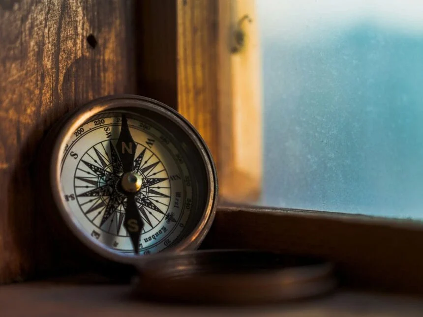 Close-up of a vintage compass resting on a wooden windowsill, with the needle pointing north and soft daylight filtering through frosted glass in the background. Represents the concept of defining purpose as a strategic guide for business direction and decision-making. {{brizy_dc_image_alt imageSrc=