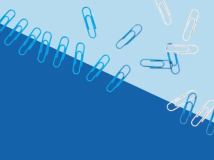 Scattered blue and white paper clips on a two-tone background, symbolising team misalignment, lack of cohesion, and disorganised collaboration. {{brizy_dc_image_alt imageSrc=