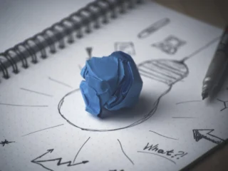 A lightbulb sketch and crumpled blue paper in a notebook, symbolizing the creative foundations of purpose-led strategic planning.